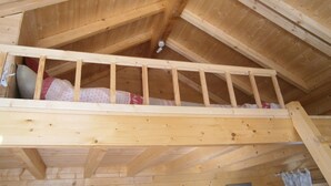 Un lit mezzanine en bois avec une échelle, des poutres en bois et un ventilateur de plafond, dans une pièce dont le plafond est en pente et également en bois.