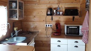 Une cuisine compacte avec des murs en bois, un évier, une cuisinière, un four à micro-ondes et un petit placard.