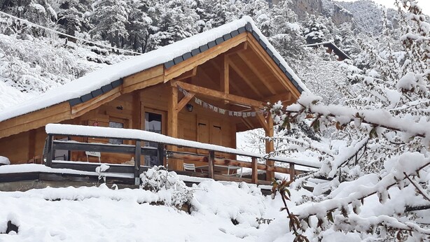 Une cabane en bois avec un toit enneigé et une terrasse en bois.