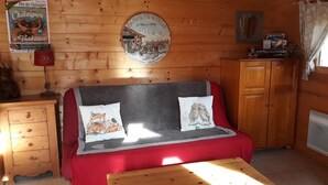 L’intérieur chaleureux d’un chalet avec un canapé rouge, des meubles en bois et une horloge fixée au mur.