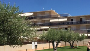 A multi-story building with balconies, a grassy courtyard, and a tree.