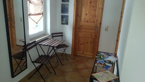 Una habitación pequeña con una puerta de madera, una ventana con cortina, una mesa con un mapa y una silla.