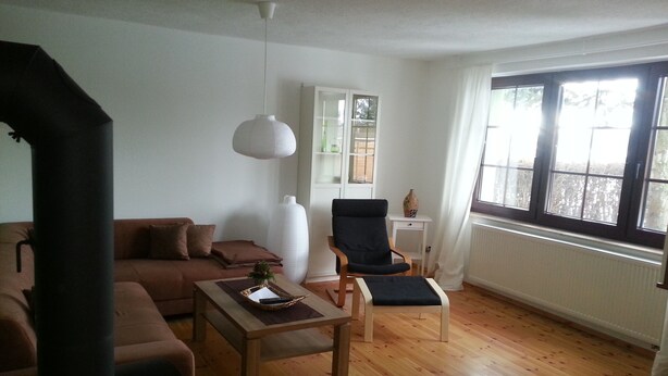 Una sala de estar con un sofá marrón, una mesa de centro de madera, un sillón negro y un jarrón blanco.