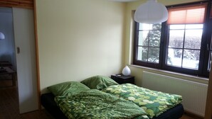 Un dormitorio con cama, mesita de noche, ventana con persianas y radiador.