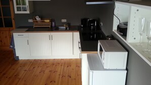 Una cocina compacta con armarios blancos, microondas, cafetera y pileta.