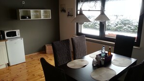 Cocina pequeña equipada con microondas, refrigerador y mesa de comedor con sillas. Se ve una ventana con vistas a árboles.