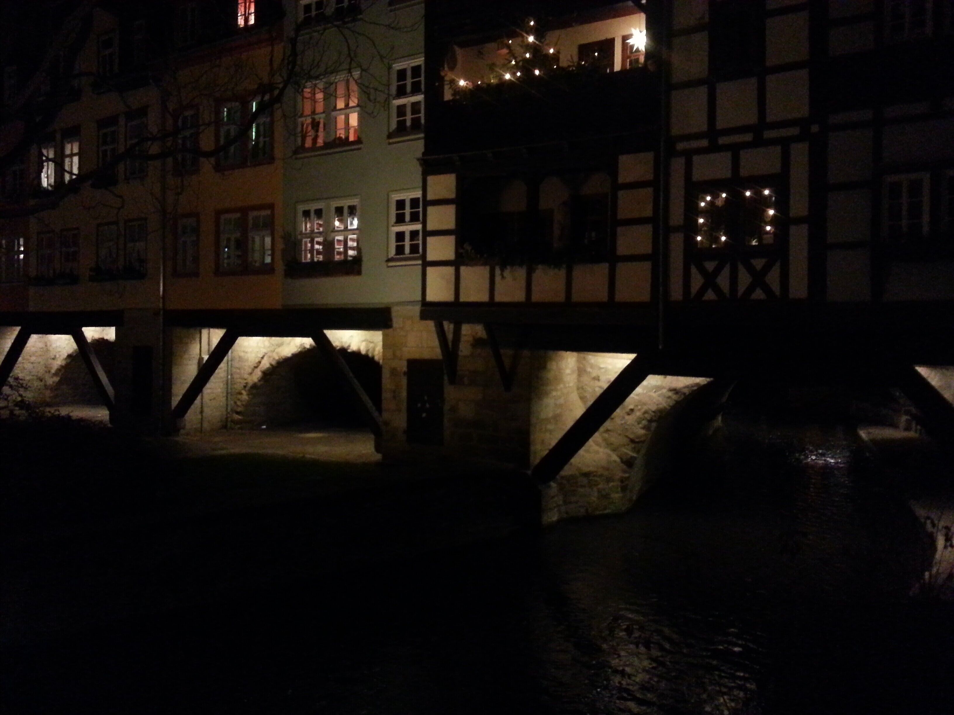 A nighttime view of a historic building with illuminated windows and a stone bridge.