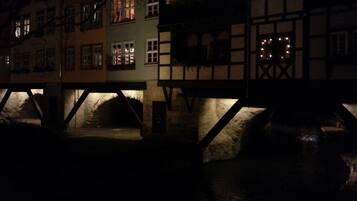 Ein beleuchtetes historisches Gebäude bei Nacht, mit leuchtenden Fenstern und einer Stebrücke.