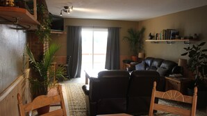 A living room with a wooden table, two chairs, a sofa, and a TV. There are plants, a bookshelf, and a window with curtains. - Near everything. Surrounded by parks, and trails. Sleeps 6. Basecamp for Montana (Bozeman)