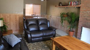 A living room with a leather sofa, a wooden coffee table, and a dining area with a table and chairs. - Near everything. Surrounded by parks, and trails. Sleeps 6. Basecamp for Montana (Bozeman)
