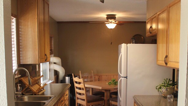 A compact kitchen with wooden cabinets, a refrigerator, a dishwasher, and a dining table with chairs. - Near everything. Surrounded by parks, and trails. Sleeps 6. Basecamp for Montana (Bozeman)