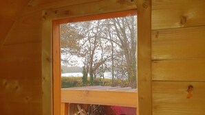 A wooden cabin with a window overlooking a lake and trees.
