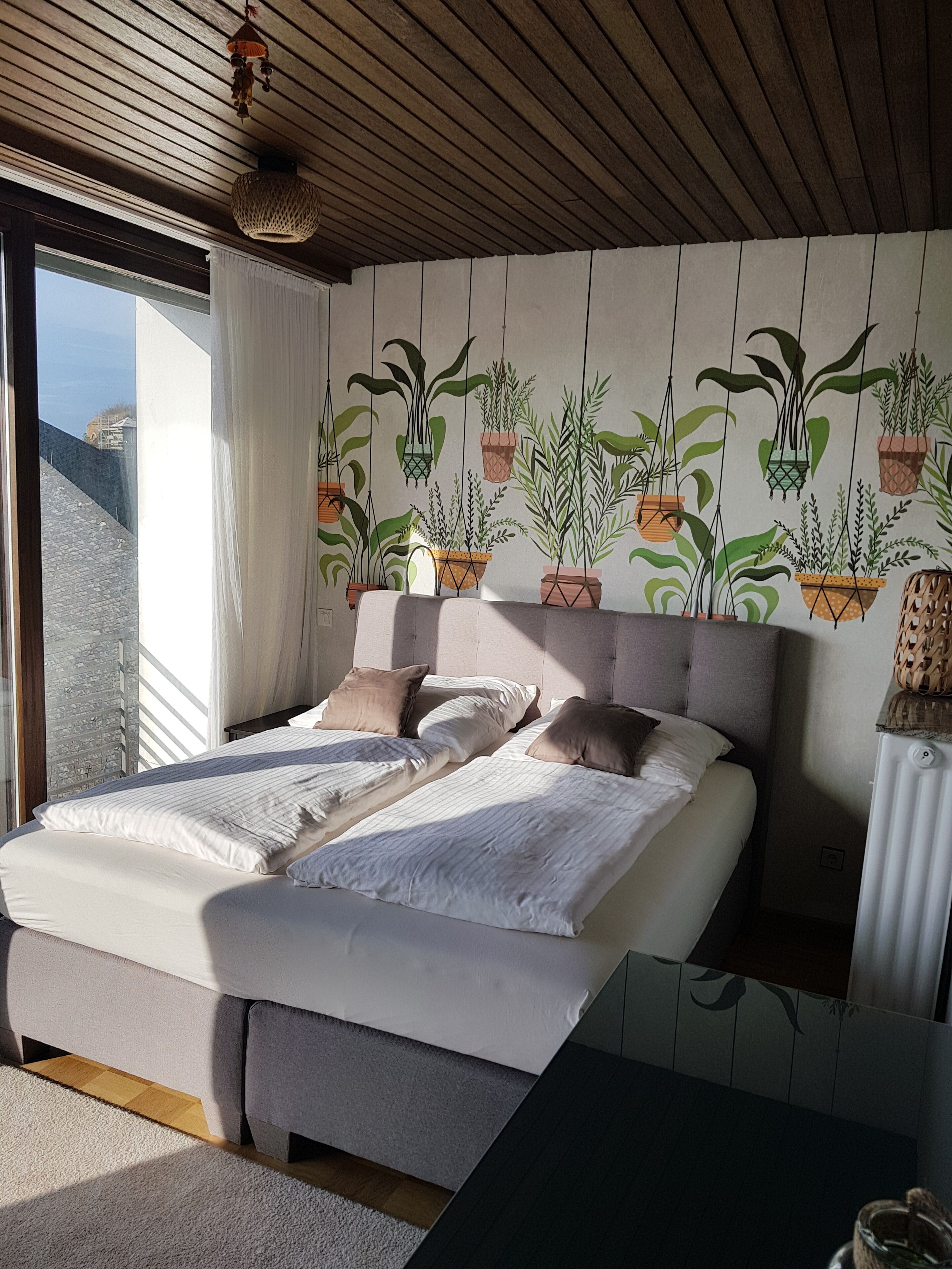 Ein Schlafzimmer mit einem großen Bett, Meerblick und einer Wand, die mit hängenden Pflanzgefäßen dekoriert ist.