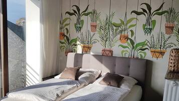Ein Schlafzimmer mit einem großen Bett, Meerblick und einer Wand, die mit hängenden Pflanzgefäßen dekoriert ist.