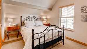 Een slaapkamer met een bed, nachtkastjes, lampen en een raam met luiken.