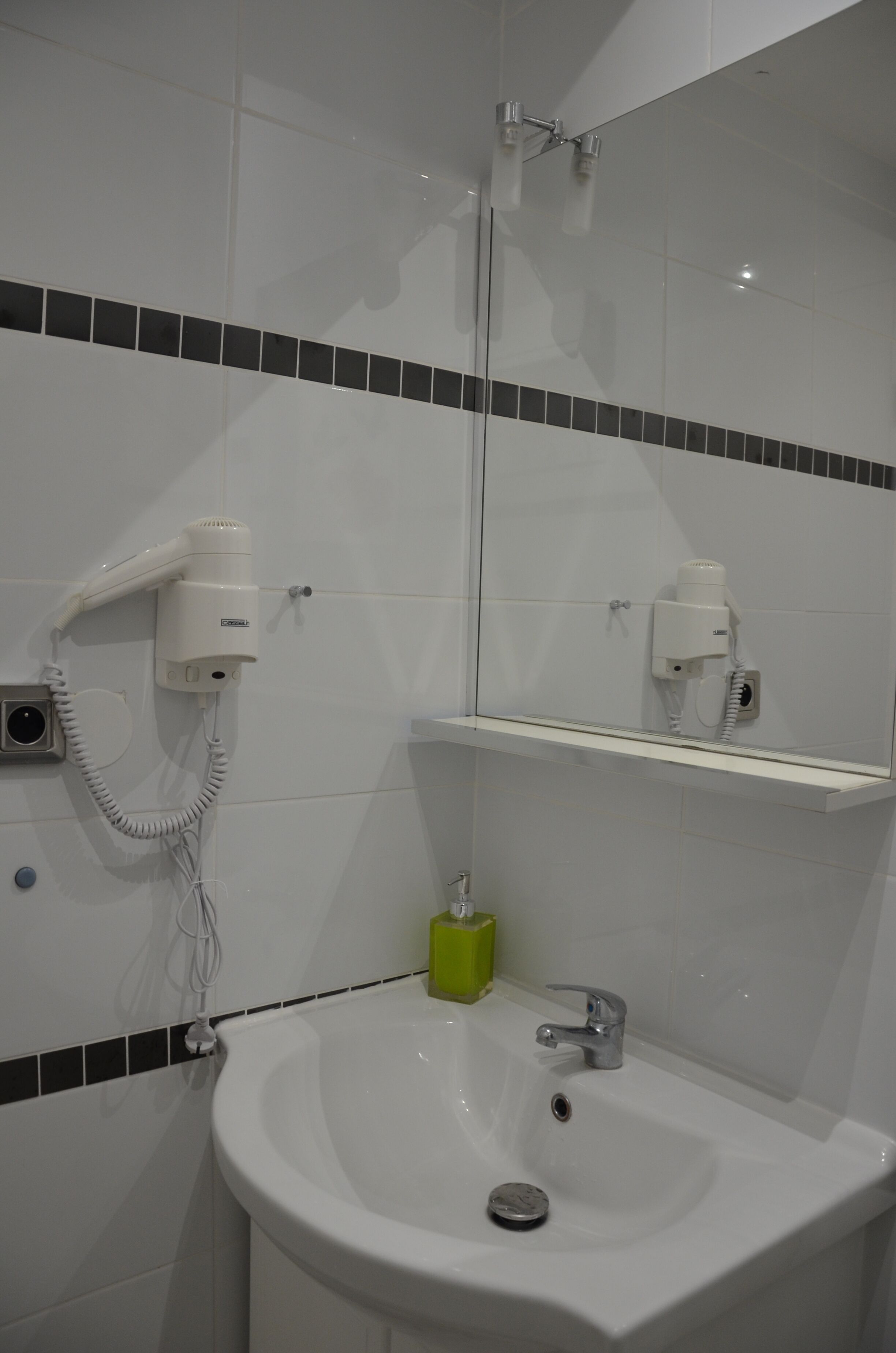 Een badkamer met een witte wastafel, een spiegel en een haardroger bevestigd aan de muur.