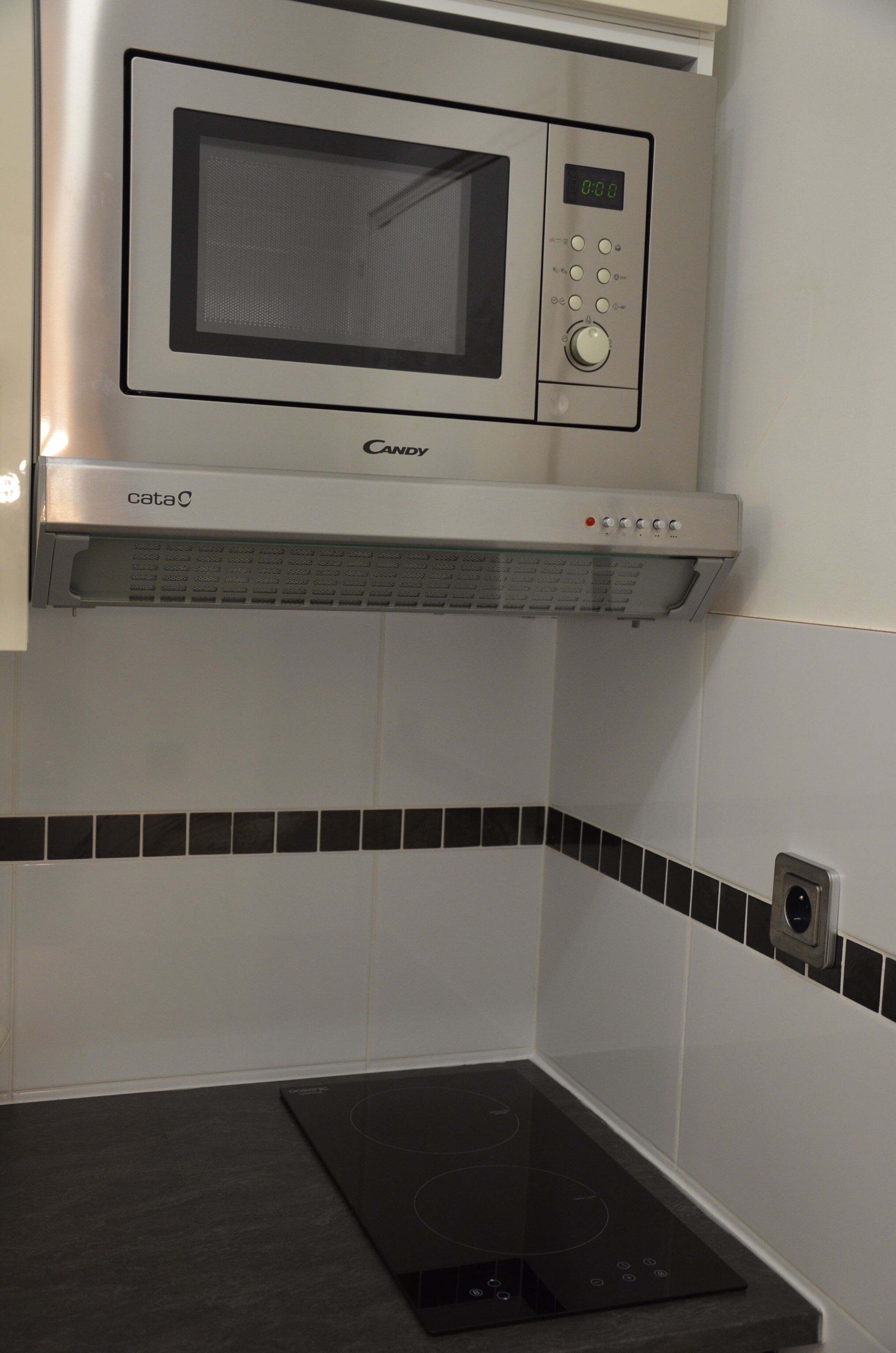 Una cocina con microondas, horno integrado y placa de inducción negra.