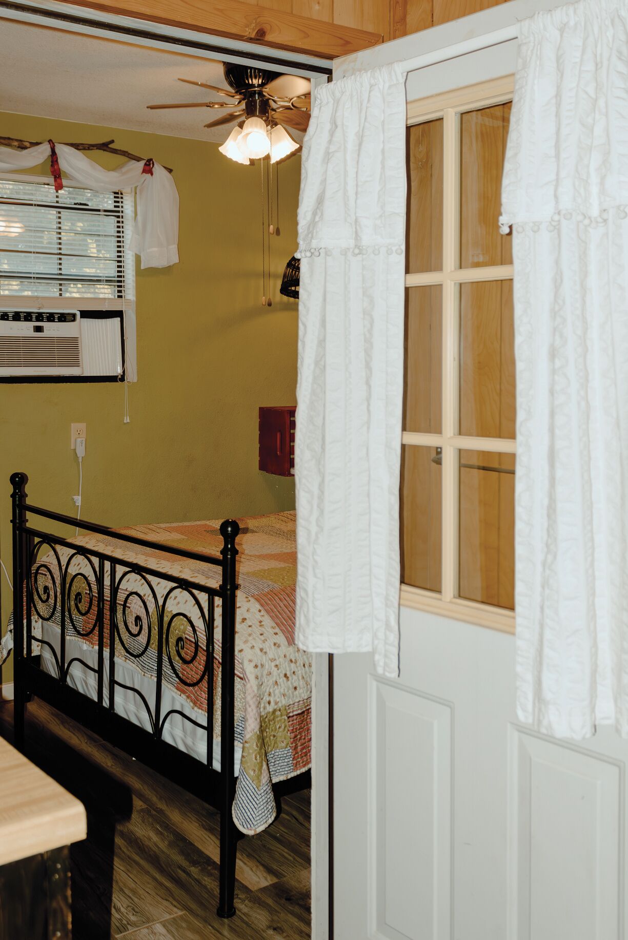 A bedroom with a bed, a ceiling fan, a window with curtains, and an air conditioning unit.