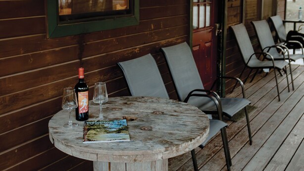 A rustic wooden deck with a round table, two chairs, and a bottle of wine.
