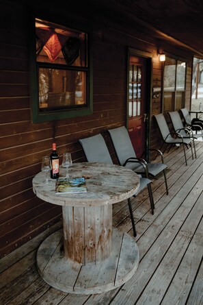 A rustic wooden deck with a round table, two chairs, and a bottle of wine. - The Bandera Cabin 3BD/1Bath @ Whiskey Mountain - Great Location! (Leakey)