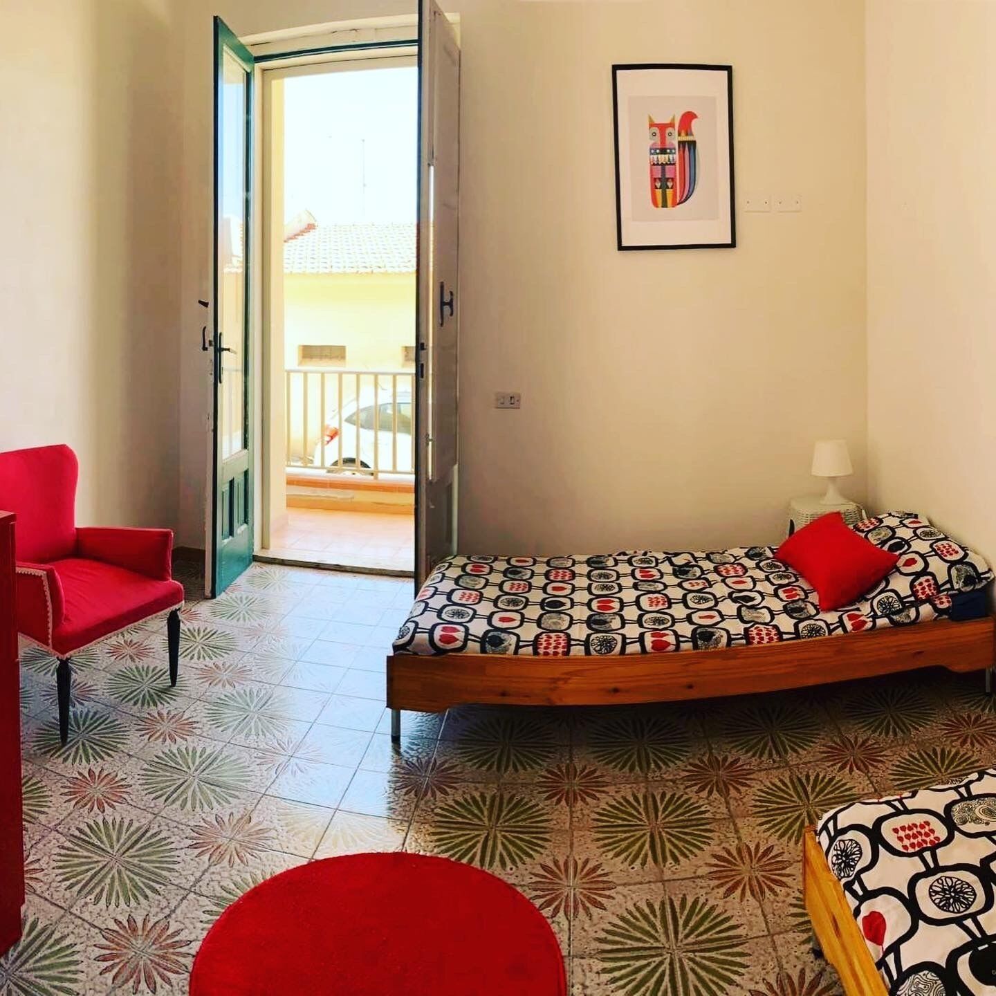 A room with a bed, a red chair, and a door leading to a balcony.