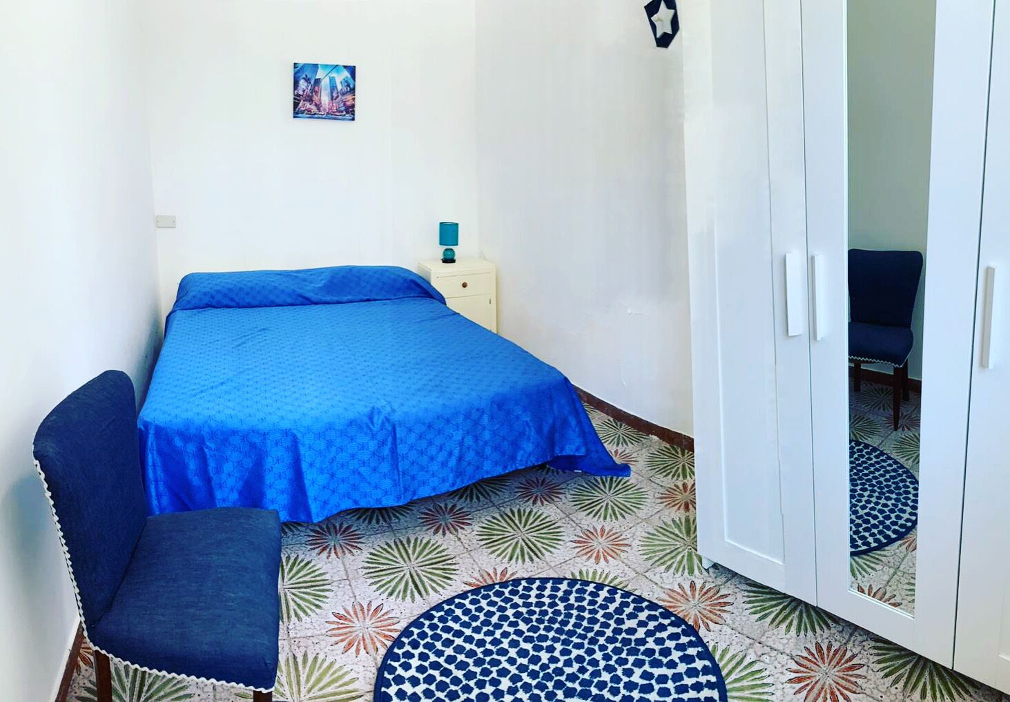 A small bedroom with a bed, a chair, a nightstand, and a wardrobe.