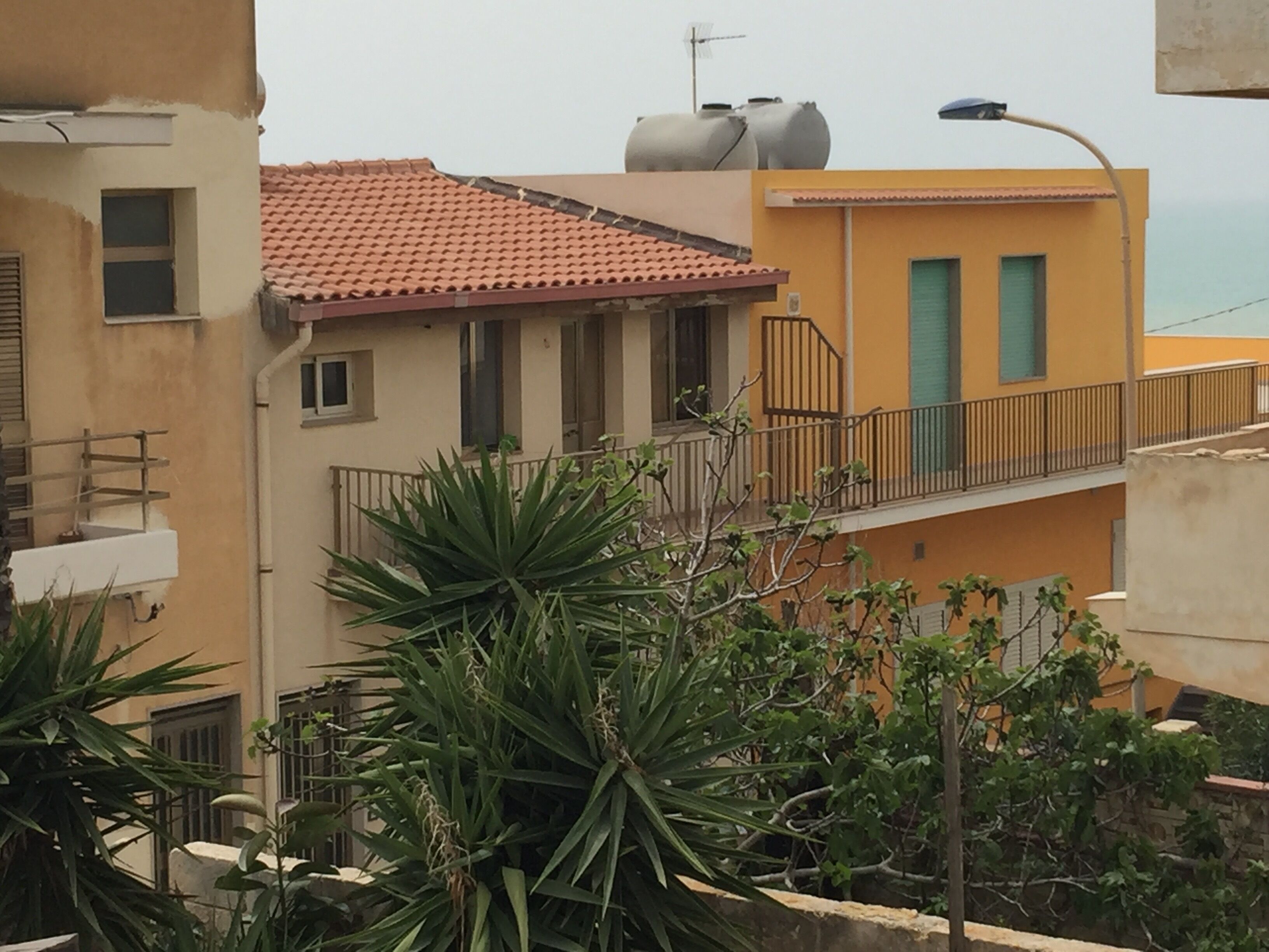 Un edificio residenziale con tetto in tegole rosse, un balcone con ringhiera in metallo e facciata gialla.