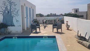 Un área de piscina en la azotea con un mural, mobiliario exterior y vistas de los edificios circundantes.