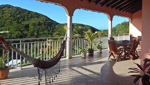 Eine überdachte Terrasse mit einer Hängematte, Topfpflanzen und einem Tisch mit Stühlen.