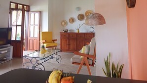 Ein geräumiges Wohnzimmer mit hoher Decke, einem Holzschrank, einem gelben Sessel und einem Glastisch mit Früchten.