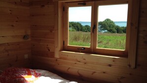 Une chambre dans un chalet en bois, avec un lit, une fenêtre donnant sur un lac et des arbres, et un ventilateur de plafond.