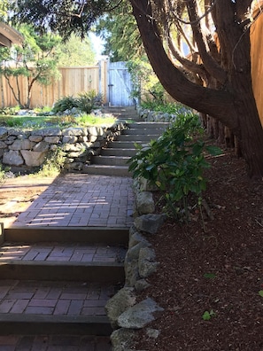 Steps lead to a serene garden entrance surrounded by lush greenery and a large tree.
