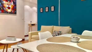 A modern living room with a teal accent wall, a beige sofa, and a white coffee table with woven placemats.