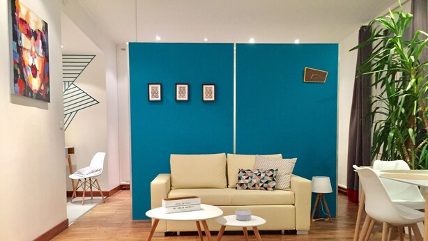 A modern living room with a teal accent wall, a sofa, a coffee table, and a dining area with chairs.