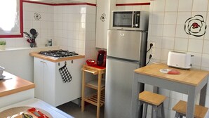 A compact kitchen with a gas stove, microwave, refrigerator, and a small table with stools.