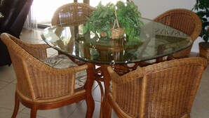 A dining area with a glass-top table surrounded by wicker chairs, a hanging light fixture, and a poster of Sarasota, Florida. - Siesta Key 2 Bedroom Condo  (Siesta Key)