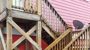 Una escalera de madera que lleva a una terraza, con un edificio rojo al fondo.