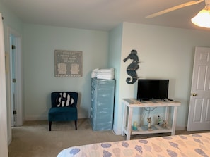 Une chambre à coucher comprenant un lit, une chaise, une commode, un meuble pour la télévision et une porte.