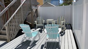 Una terraza de madera con dos sillas Adirondack y una mesita, rodeada por una valla blanca.