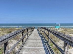 A wooden boardwalk leading to a beach with a lifeguard tower in the distance. - Buckeye Beach House 2 blocks from the beach (Carolina Beach)