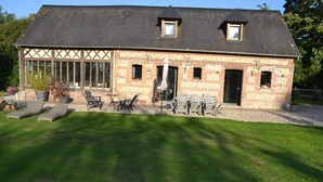 Ein Backsteinhaus mit einer großen Terrasse, Sitzgelegenheiten im Freien und einem kleinen Garten.