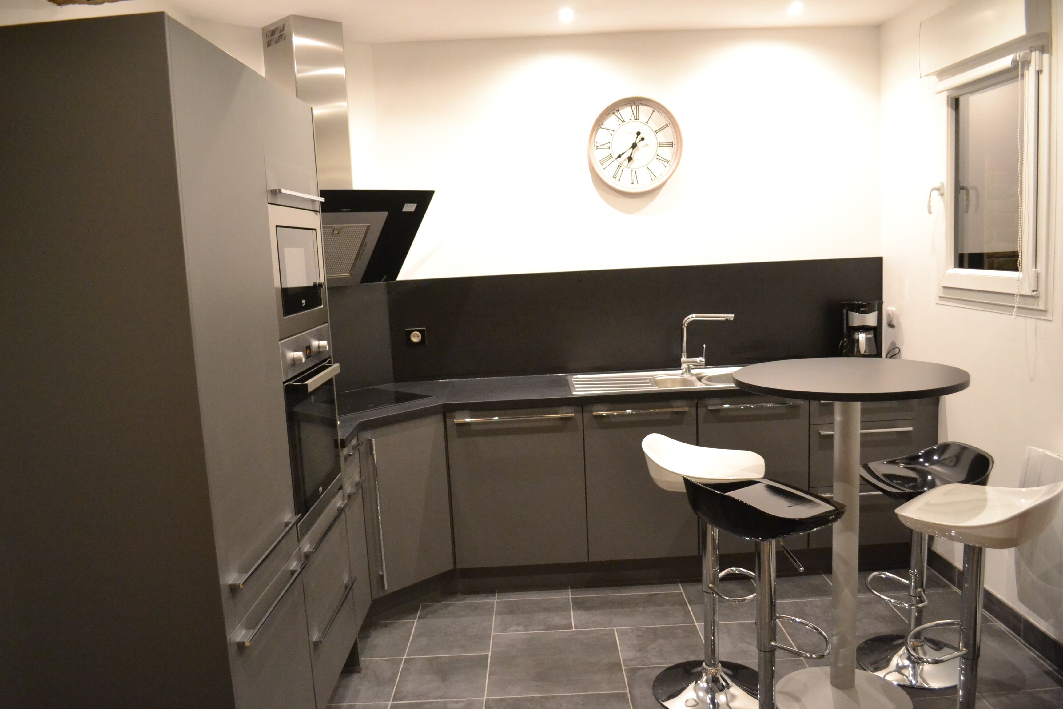 A modern kitchen with a built-in oven, microwave, and sink. There are two bar stools and a round table.