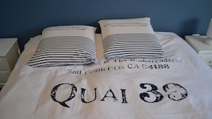 Ein Bett mit gestreiftem Kopfkissen und einer Tagesdecke mit dem Aufdruck "QUAI 33" und "San Francisco, CA 94133".
