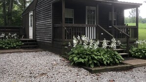 A log cabin with a porch, a front door, and a small garden area with white flowers. - Lakeside Cottage, Fishing, Canoe & Kayak, Pet Friendly, Golf and Hiking Nearby (Crofton)