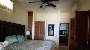 Une chambre à coucher comprenant un lit, un ventilateur de plafond, une table de chevet, une lampe, une armoire et un miroir.