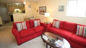 A living room with two red sofas, a glass coffee table, and a kitchen in the background. - Cozy, Private, Gated,  Hilton Head Location with Great Views. Steps to the beach (Hilton Head Island)
