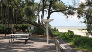 A picnic area with benches and a picnic table, surrounded by trees and a view of the beach. - Cozy, Private, Gated,  Hilton Head Location with Great Views. Steps to the beach (Hilton Head Island)
