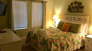 A bedroom with a bed, bedside table, lamp, and a desk with a remote control. - Cozy, Private, Gated,  Hilton Head Location with Great Views. Steps to the beach (Hilton Head Island)