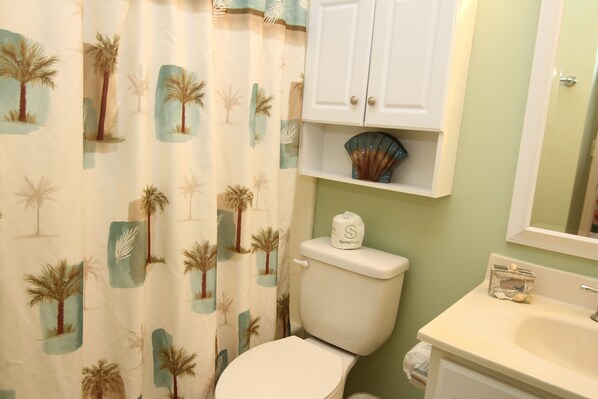 A bathroom with a toilet, a sink, a cabinet, and a shower curtain with palm tree patterns. - Cozy, Private, Gated, Hilton Head Location with Great Views. Steps to the beach (Hilton Head Island)
