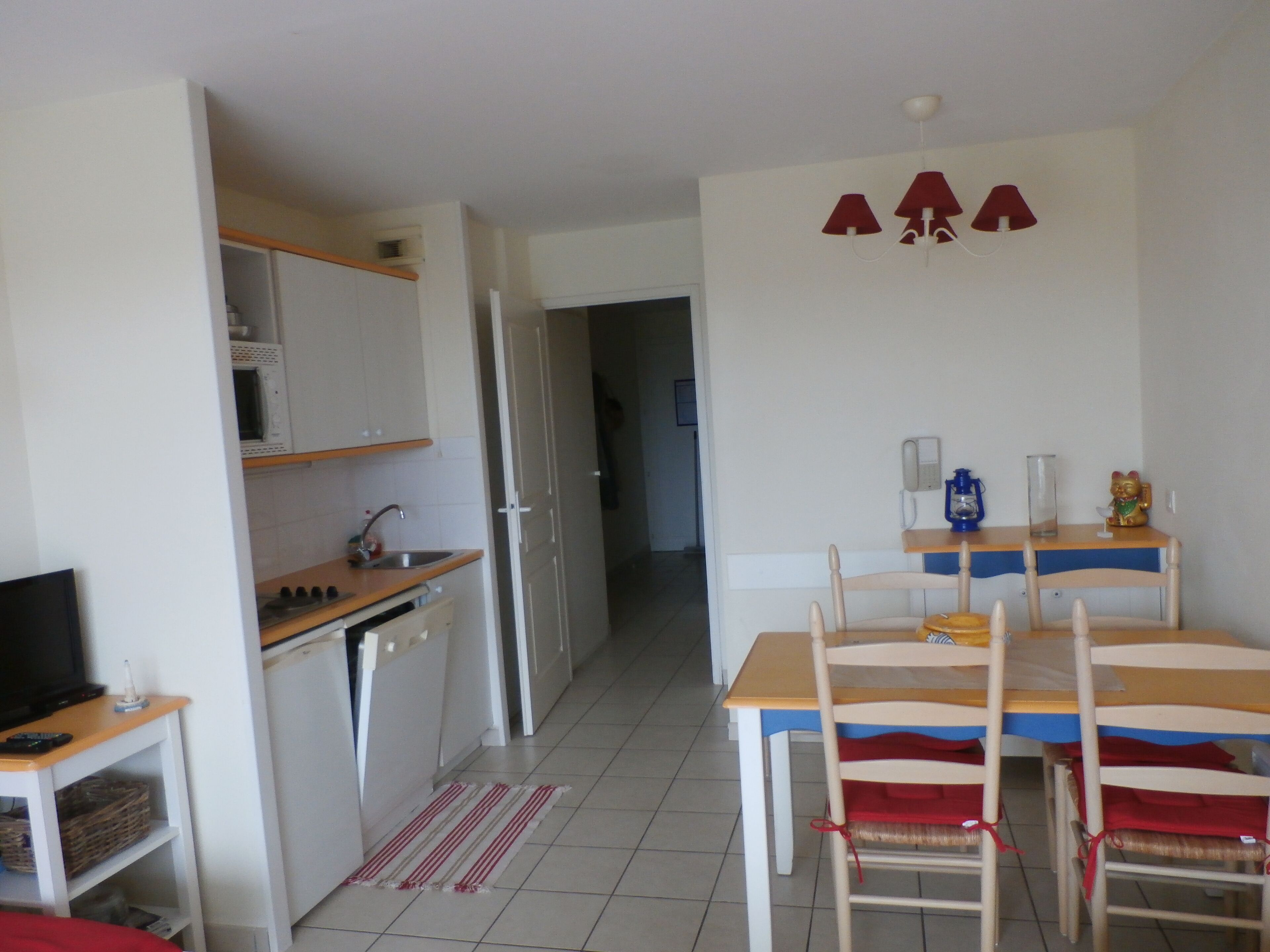 Un espacio habitable compacto con kitchenette, una zona de comedor con dos sillas, una mesa pequeña y un televisor sobre un soporte.